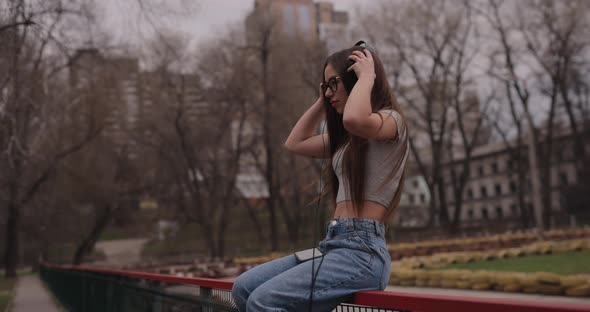 Happy Girl Listening to Music in Headphones Sitting on Fence