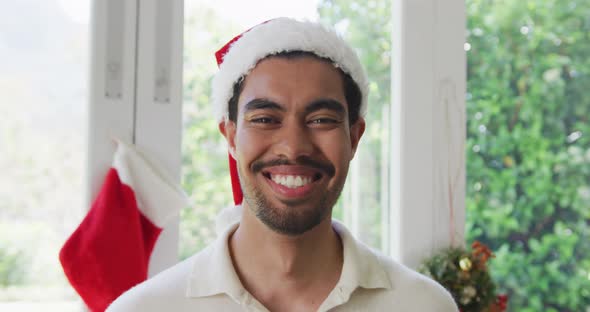 Portrait of happy biracial young man in santa hat at home during christmas