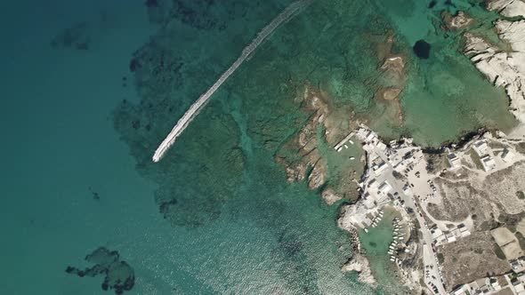 Circling shot of a small Greek town as a jet ski rushes through the crystal-clear waters of the Medi