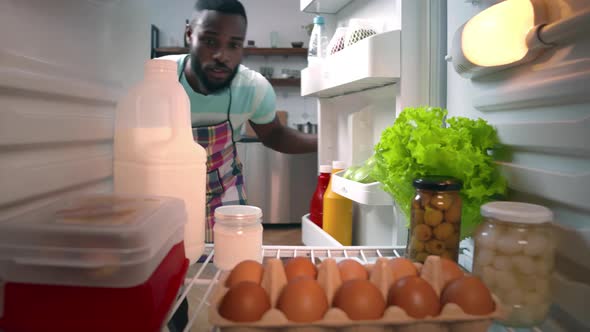 Young AfricanAmerican Ethnicity Man in Apron Taking Food From Fridge to Cook Dinner