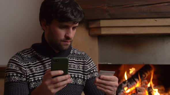 Man Shopping Online Using Smartphone at Home Sitting By the Fireplace