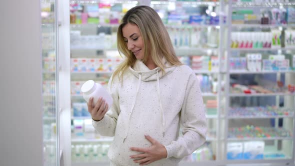 Portrait of Happy Pregnant Beautiful Woman Advertising Pills Standing in Pharmacy Indoors