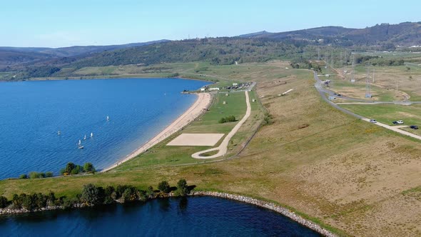 Lake beach with people sunbathing and bathing, small sailboats sailing, garden and walking area. Dro