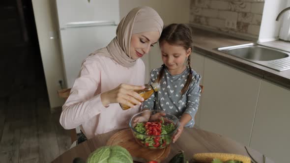 Portrait of Smiling Mom in Hijab and Little Caucasian Daughter Adds Salt to the Salad