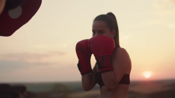 Woman in Boxing Gloves Trains with Coach in Paws Nature at Sunset Front View
