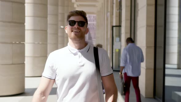 Smiling Caucasian Man in Sunglasses Walking Outside Modern Business Center Looking Around