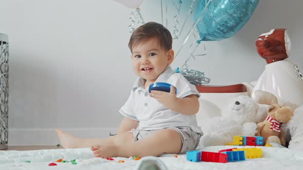 Little Baby Boy Sitting On The Floor Smiling And Playing With Toys