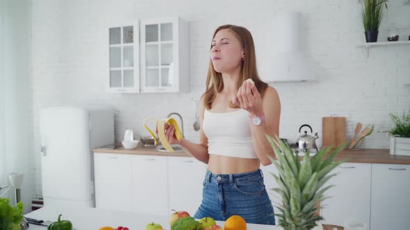 Slim woman with banana in the kitchen. Beautiful girl in the modern light kitchen.