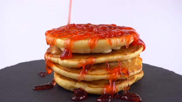Pancakes with strawberry topping on a white background. Pancake lies on a black slate round stone.
