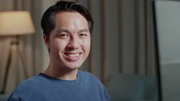 Close Up Of Asian Male Engineer With House Model Smiling To The Camera While Working On A Desktop