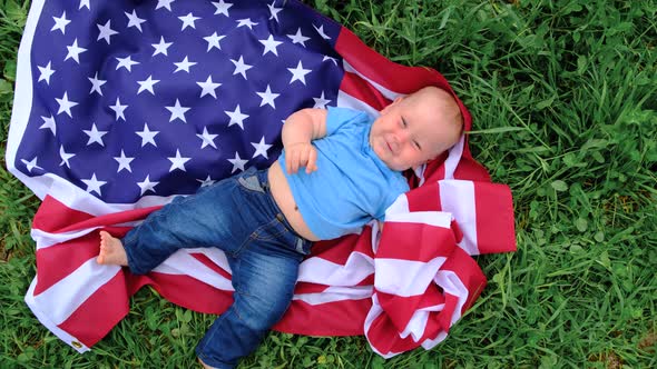 Excited Baby Lying on National USA Flag Outdoors Over Summer Green Grass American Flag Country