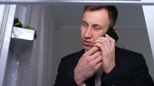 Man Talks on Phone Eating Sandwich with Butter Near Fridge