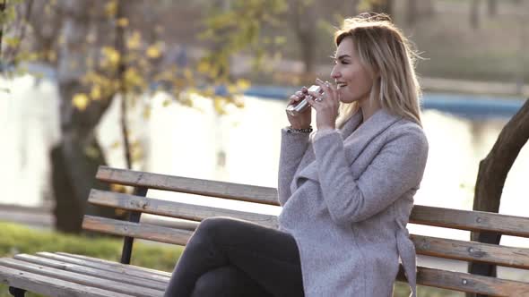 Young Beautiful Business Woman Drinks Alcohol Whiskey on Nature in the Park at Sunset After Hard