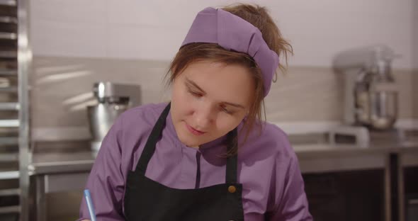 Girl Confectioner Sitting In A Confectionery Makes A Sketch For Desserts