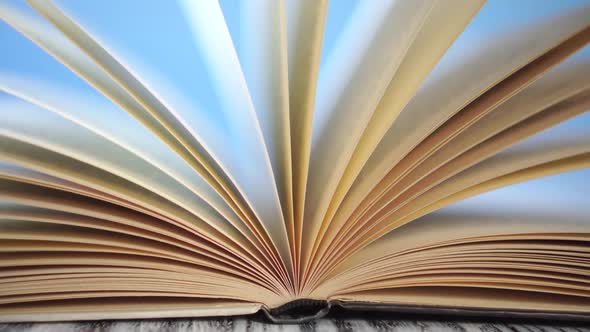 pages of an old hardcover book sway from the wind on an antique wooden table.