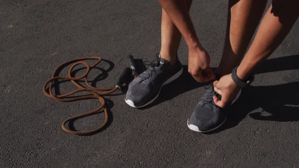 Low section of african american man exercising in city with skipping rope, tying shoelaces in street