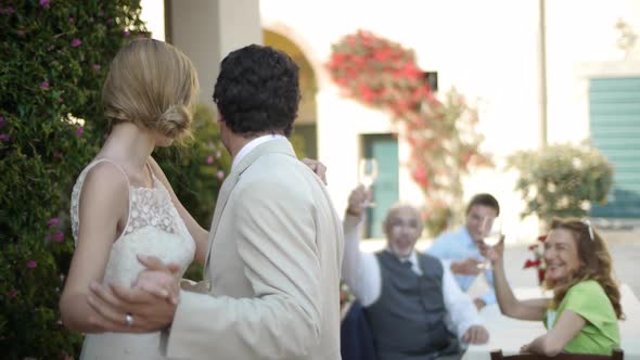 Bride and groom dancing and kissing, wedding guests toast them