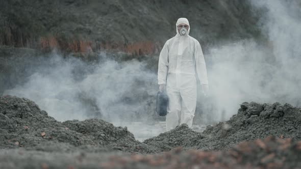 Lab technician in a mask and chemical protective suit walking on dry ground