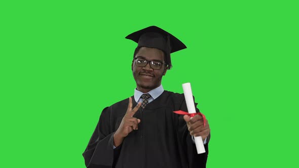 Happy African American Male Student in Graduation Robe Posing with Diploma for Camera on a Green