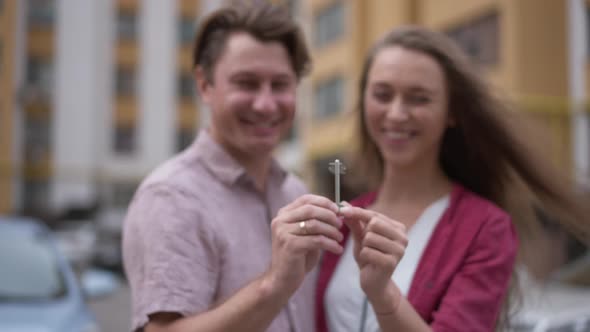 Closeup Key in Couple Hands with Blurred Caucasian Man and Woman Talking Smiling at Background