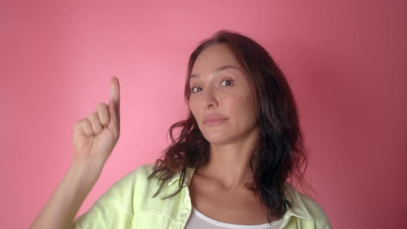 Portrait of Young Woman Shows Finger Up on Empty Space on a Pink Background