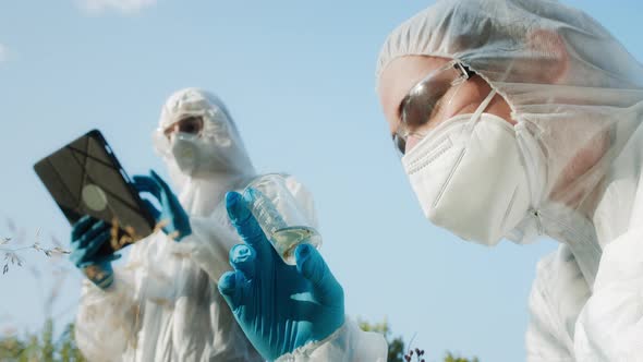 Chemists Wearing Ppe Suits Taking Sample of Water for Toxicity Testing Typing in Gadget Tablet