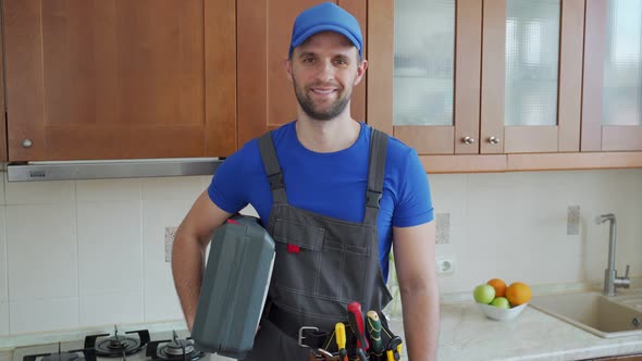 Repairman Holds a Suitcase of Tools in the Kitchen and Looks at the Camera