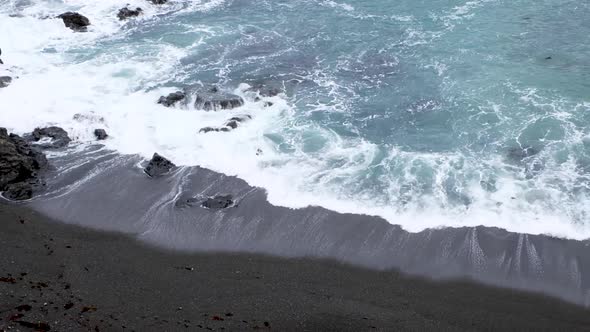 Whitewash waves rolling and breaking on black sand beach in remote bay in capital Wellington, New Ze