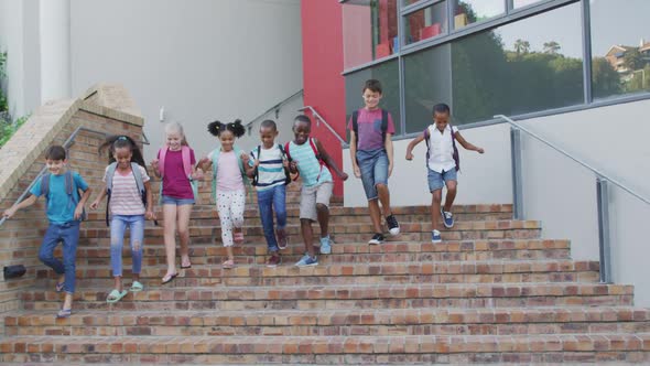 Diverse group of schoolchildren wearing backpacks smiling and running downstairs after school