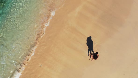 Young couple in love kissing on quiet exotic beach with sand washed gently by turquoise sea waves in