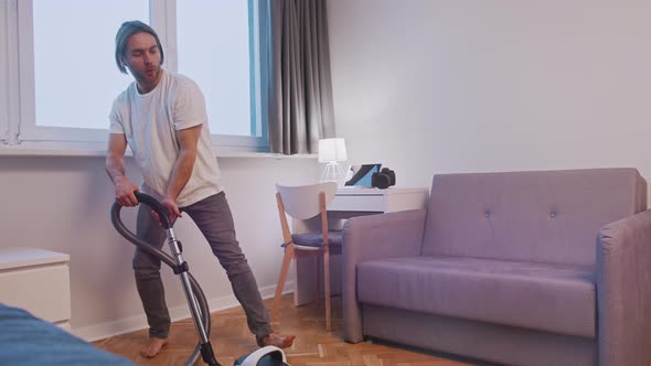 Young Caucasian Man Having Fun During Cleaning House Playing with Vacuum Cleaner at Living Room