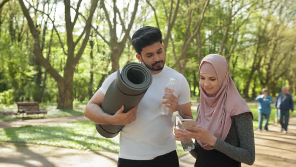 Young Woman in Sportswear and Hijab Using Modern Smartphone While Handsome