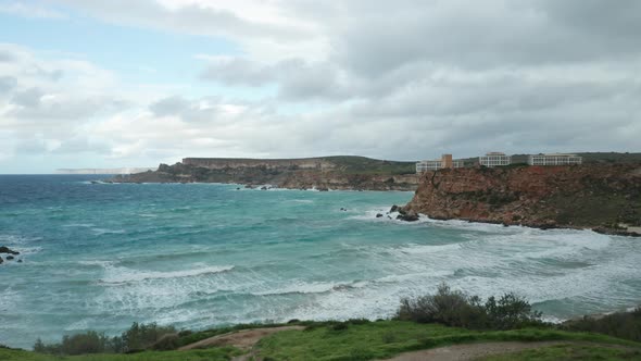 AERIAL: Ghajn Tuffieha Bay on a Gloomy but Bright Day with Sea Roaring and Splashing into Shore