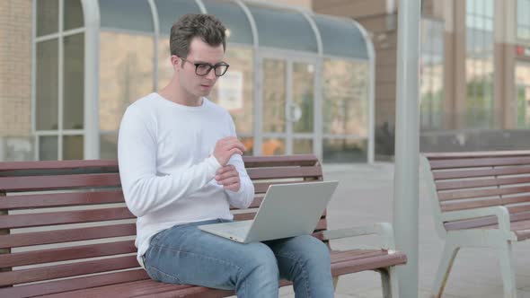 Young Man with Wrist Pain Using Laptop While Sitting on Bench