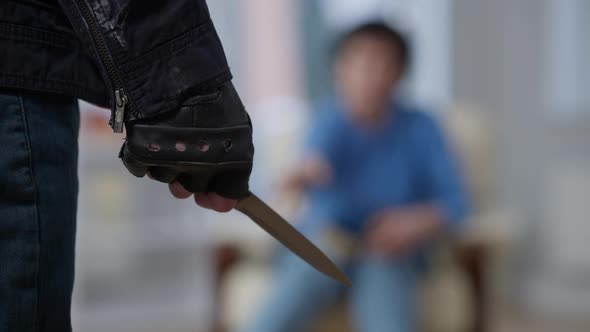 Closeup of Knife in Male Caucasian Hand with Blurred Robbery Victim at Background