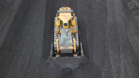 Bulldozer tractor collecting black coal on supply field of thermoelectric power station