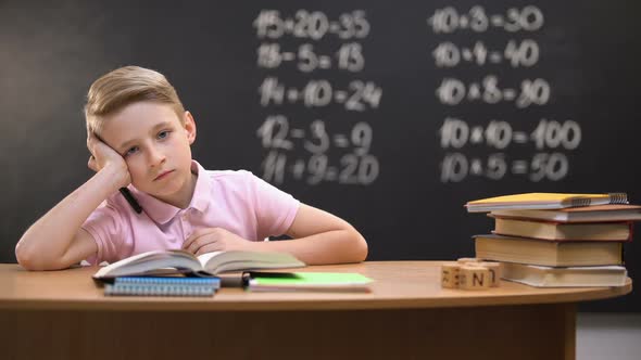 Overloaded Schoolboy Sitting at Desk and Trying to Solve Task Difficult Equation