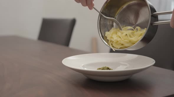 Slow Motion Man Pour Pesto Fettuccine From Saucepan To White Pasta Plate on Walnut Table