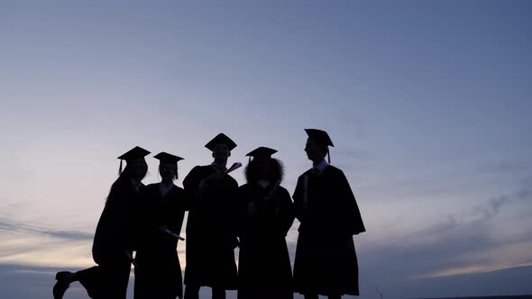 Silhouette of Graduates with Certificates on a Sunset Background