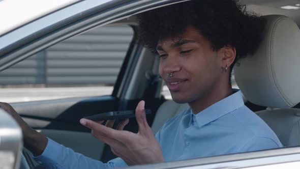 Focused African American Male Professional Recording Voice Message to Smartphone in Modern Car
