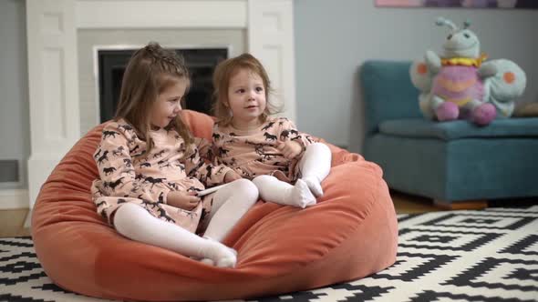 Picture of Little Curious Children in Dresses Sitting on Bean Bag Chair in Living Room and Using