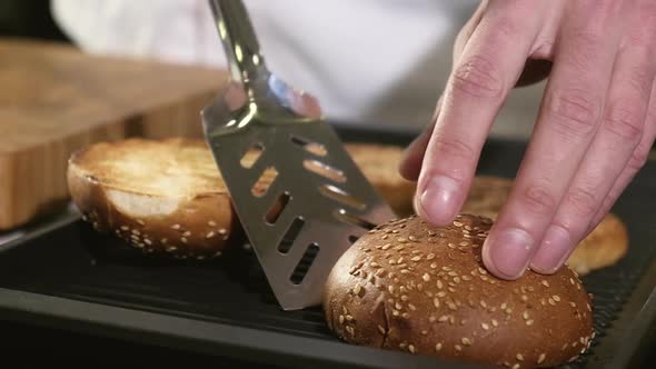 Professional male chef roasts and turns sliced buns on hot grill pan.