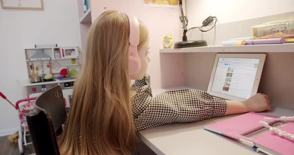 Little Girl in the Children's Room with Pink Headphones Using Digital Tablet