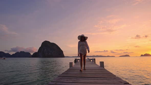 Woman Walking Along Wooden Pier As Sun Sets Over The Ocean