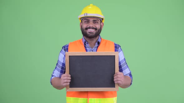 Happy Young Overweight Bearded Indian Man Construction Worker Talking While Holding Blackboard