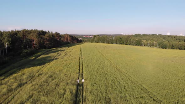 Unrecognizable Young Man and Woman Run Down Road in Green Field Aerial View