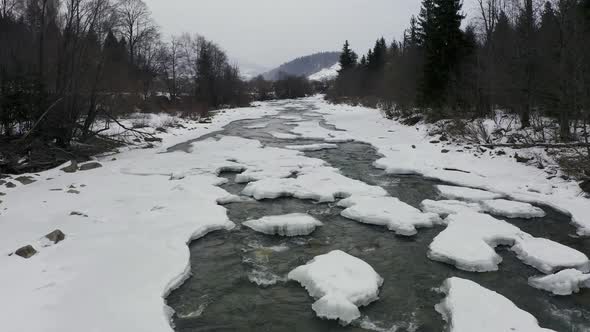 Aerial View in Winter on a Mountain River with a Forest During a Snowfall