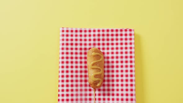 Video of corn dog with mustard on a yellow surface