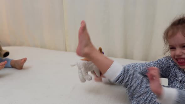 Two Smiling Preschool Toddler Children In Pajamas Playing With Teddy Bear on Bed