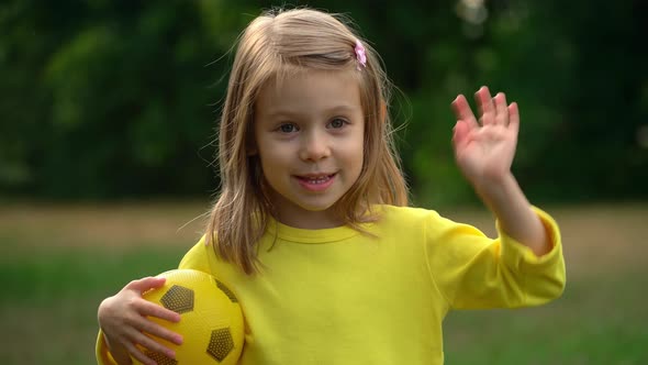 Little Child with Soccer Ball Looks at Camera Smiles and Laughs in Summer Park